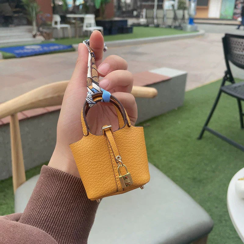 A hand holds a small mustard yellow mini handbag with a patterned wrist strap in an outdoor setting.
