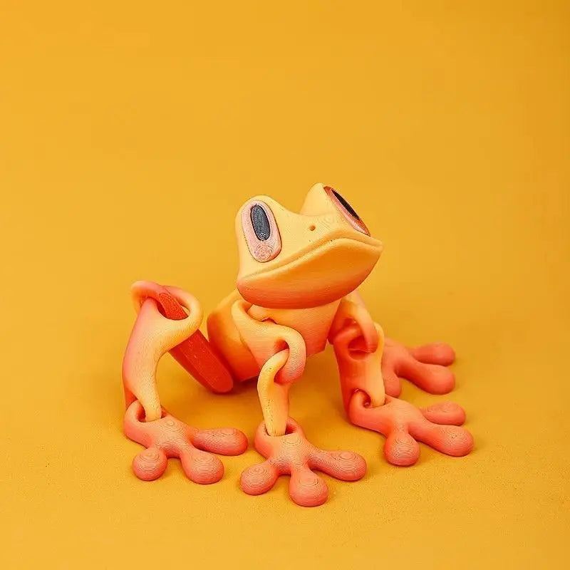 A small, orange tree frog ornament with large eyes is displayed against a plain yellow background.