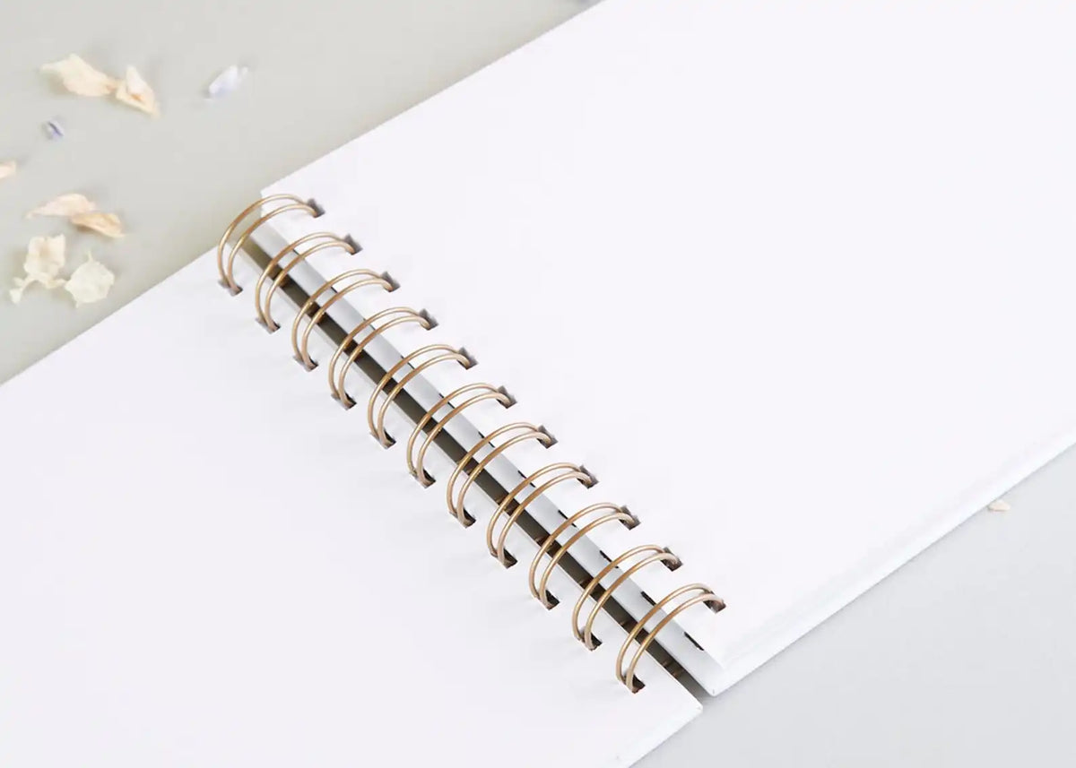 A white spiral-bound notebook with gold-colored rings lies on a light gray surface.