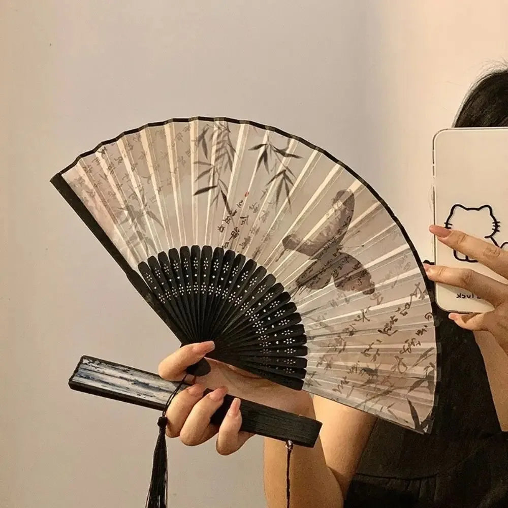 A person holds an antique style bamboo folding hand fan with delicate leaf designs.