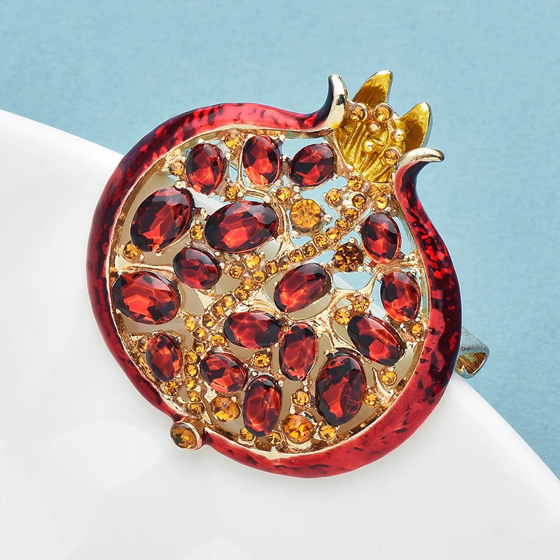 A detailed crystal pomegranate brooch pin featuring deep red stones and gold accents.