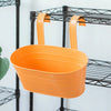 An orange modern boho metal hanging planter is displayed on a black wire shelving unit.