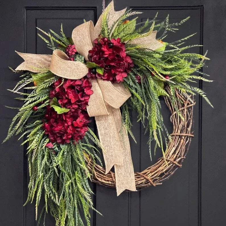 A rustic wreath made of green foliage and deep red berries tied with a natural burlap bow, suitable for door or wall decor.