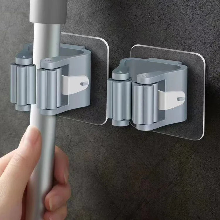 A hand is attaching an adhesive wall hook for mops and brushes to a vertical pole.