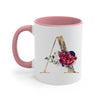 A pink ceramic coffee mug featuring a gold letter initial design surrounded by floral accents.