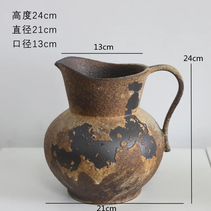 A brown ceramic pitcher or vase with a handle and decorative dark markings on its body.