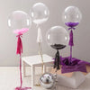 A display of clear bubble balloons in pink, purple, and silver on a white table.