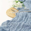 A light blue semi-sheer gauze fabric draped with ruffled texture next to a gold woven mat and silver cutlery.