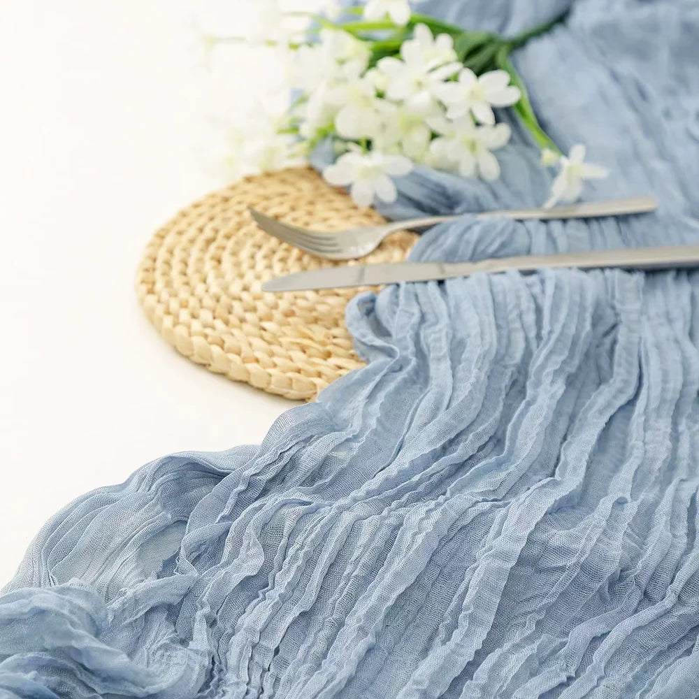 A light blue semi-sheer gauze fabric draped with ruffled texture next to a gold woven mat and silver cutlery.