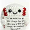 A handmade white crochet baseball bat doll with red stitching and a card that reads You are braver than you think stronger th