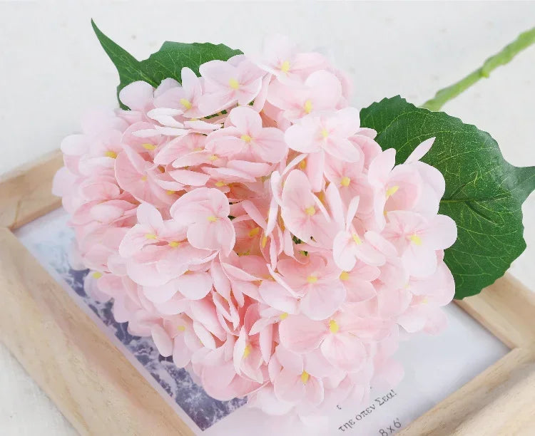 A large bouquet of pink artificial hydrangea flowers displayed on a wooden tray.