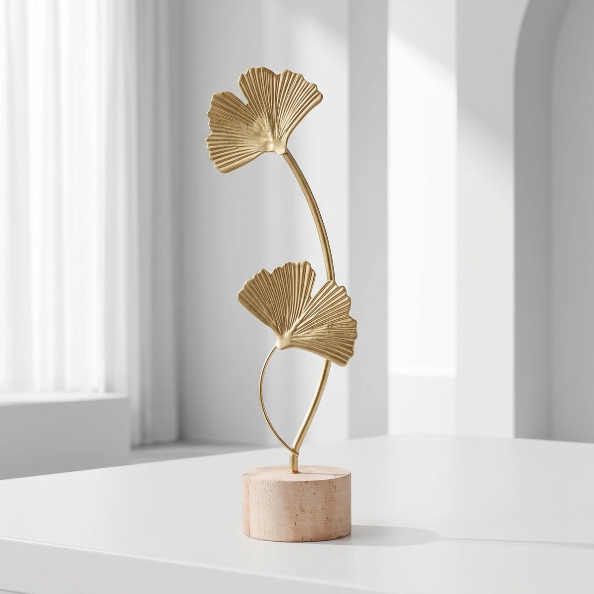 A gold-colored iron ginkgo leaf ornament set with a slender stem mounted on a light wood base.