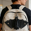 A tan backpack features a black leather bat-shaped wallet keychain with a zipper coin purse.