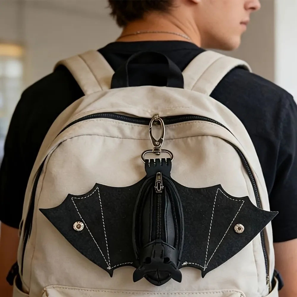 A tan backpack features a black leather bat-shaped wallet keychain with a zipper coin purse.