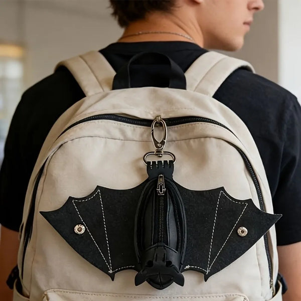 A tan backpack features a black leather bat-shaped wallet keychain with a zipper coin purse.