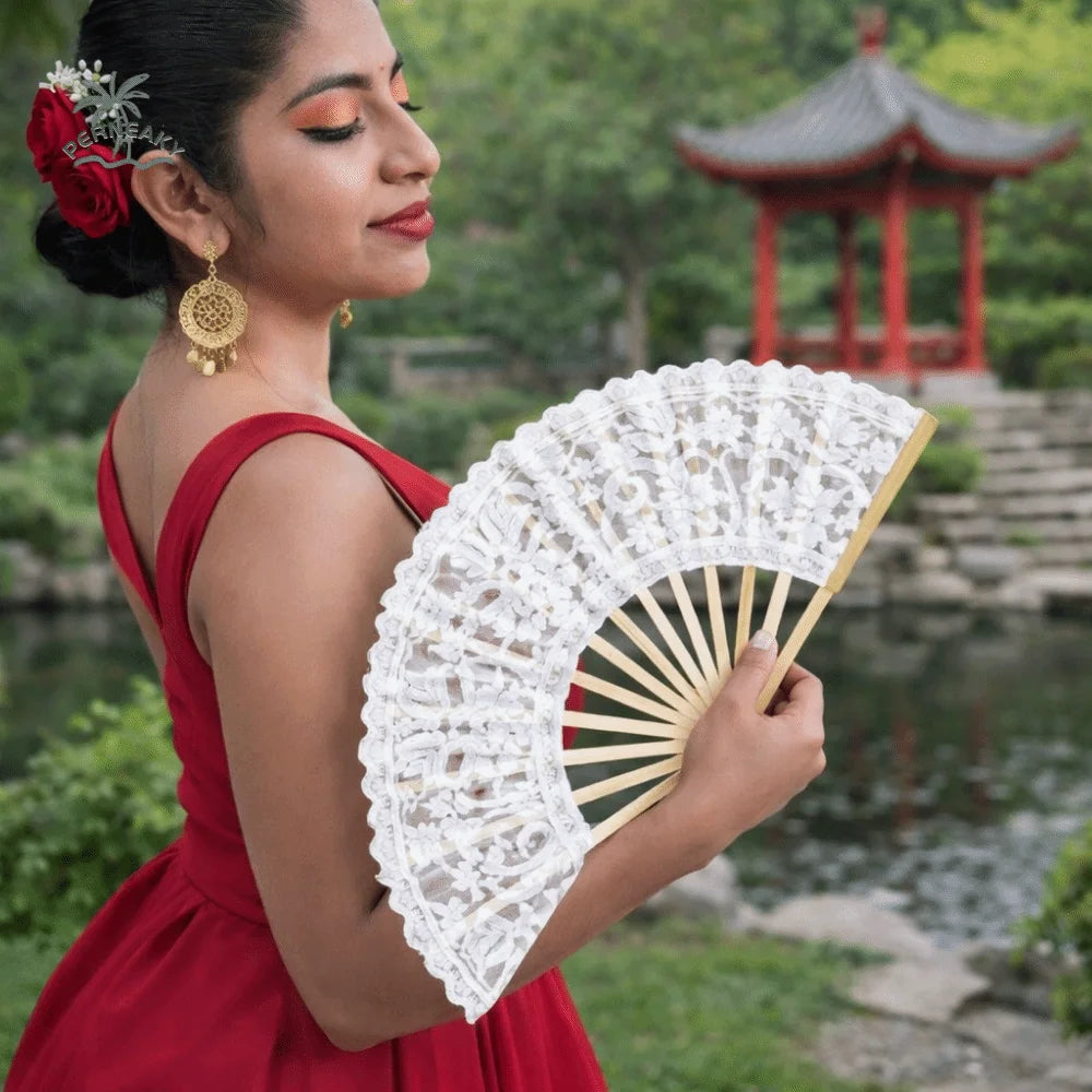 A woman in a red dress holds a vintage lace hand fan with a gold tassel pendant.