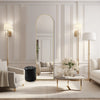 A full length arched gold mirror hangs on a white wall in a bright, elegant living room setting.