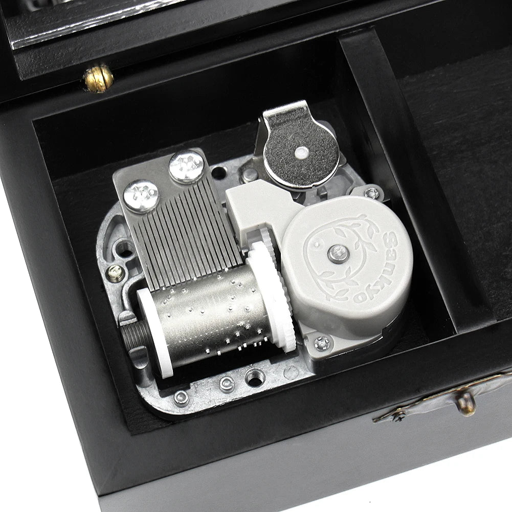 A hand-cranked wooden music box mechanism with a silver cylinder and metal components inside a black box.