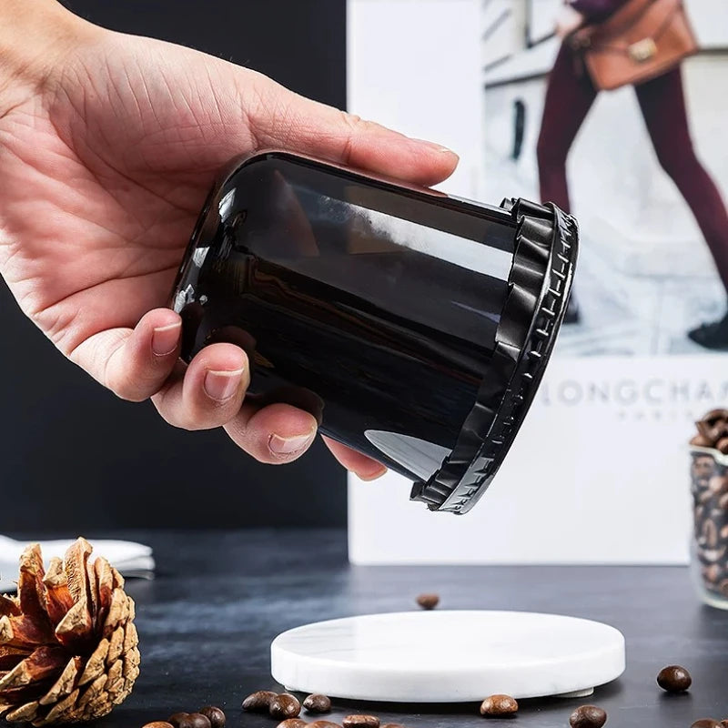 Eine Hand hält eine schwarze, transparente Einwegtasse für Getränke auf einer dunklen Oberfläche.