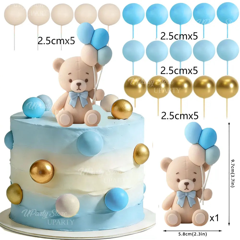 A tiered cake decorated with blue and gold balloons and a teddy bear topper set.