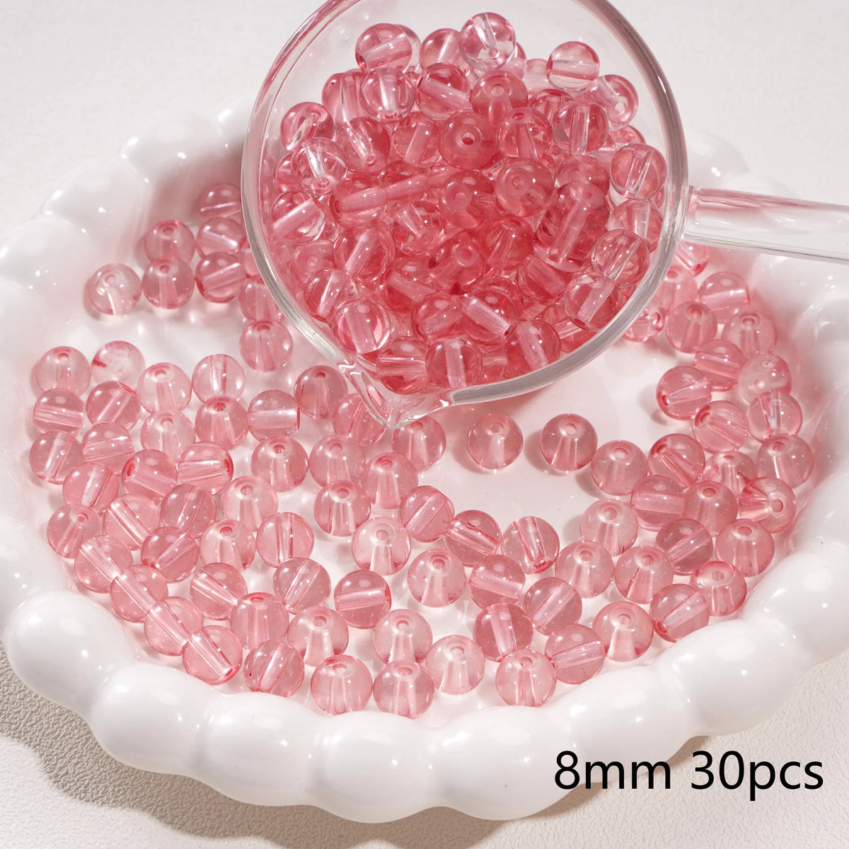 A clear glass dropper shows pink round spacer beads scattered on a white dish.