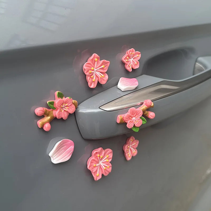 A set of pink and peach blossom-shaped ornaments decorating a gray car dashboard.