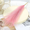 A pink artificial pampas grass bouquet displayed on a light yellow plate with natural decor elements.