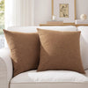 Two brown linen pillows resting on a white sofa with a framed picture in the background.