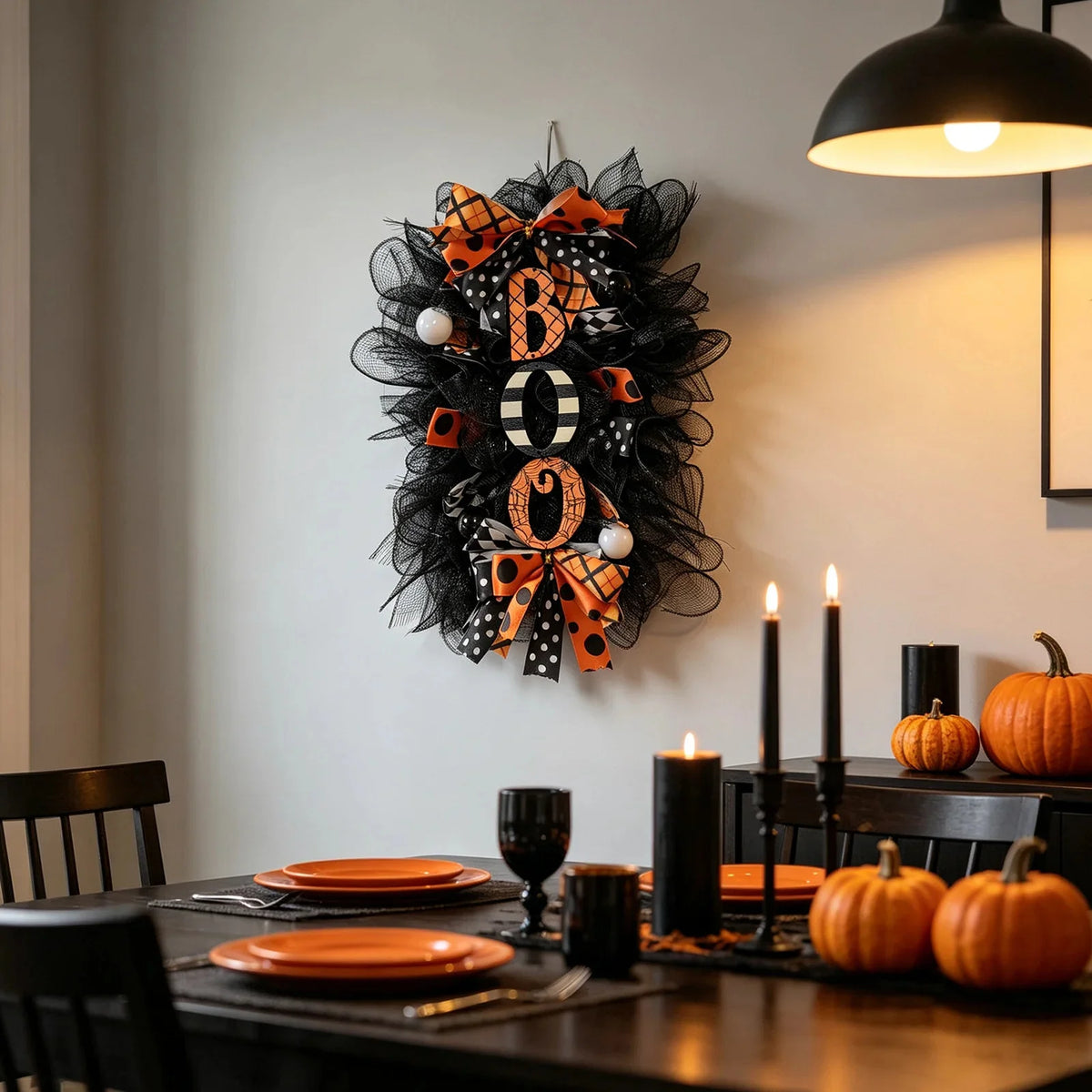 A black Halloween BOO wreath with an orange pumpkin garland hanging on a white wall.