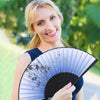 A woman holds a vintage bamboo folding hand fan with delicate silver accents against a blurred green background.