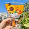 A hand holds a bouquet of handmade crochet flowers in orange and yellow tones tied with a ribbon.