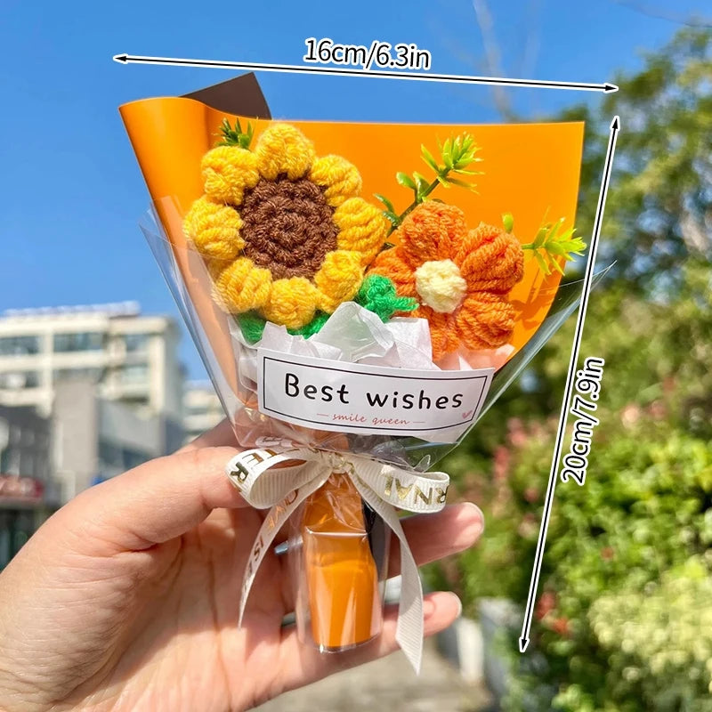 A hand holds a bouquet of handmade crochet flowers in orange and yellow tones tied with a ribbon.