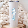 A white tumbler with light blue text that reads Sample is displayed against a background of cream-colored yarn.