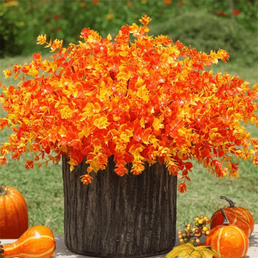 Leuchtend orangefarbene künstliche Sträucher als saisonale Dekoration vor grünem Hintergrund mit Kürbissen.