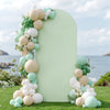 A light green arch backdrop decorated with round balloons in shades of beige, white, and mint green on a grassy outdoor setti