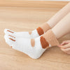A pair of white plush socks with brown cat paw prints are shown resting on a wooden surface.