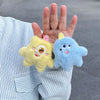 Two fuzzy plush monster keychains, one yellow and one blue, are held by a person against a striped shirt.
