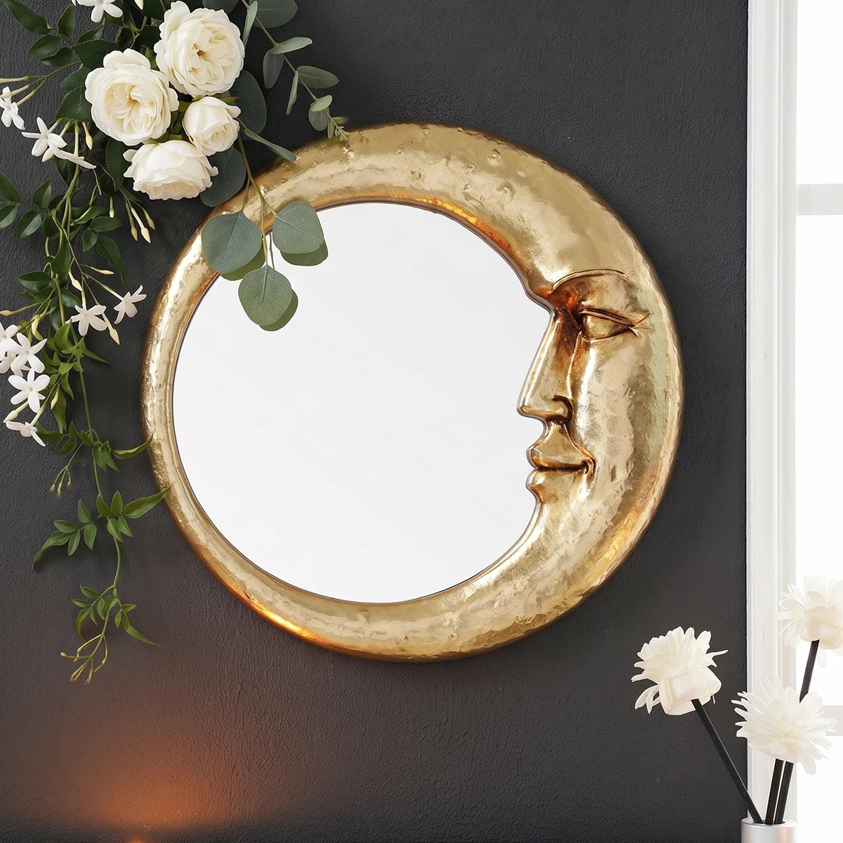A round, golden decorative wall mirror with a crescent moon face design hangs on a dark gray wall.