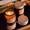 A hand-poured soy aromatherapy candle in a glass jar with a lit wick, set against a gold-edged box.