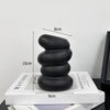 A stack of smooth black river stones on a white book, demonstrating their size.