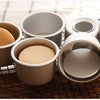 A set of five round non-stick cake molds in beige and gray are displayed on a black wire rack.