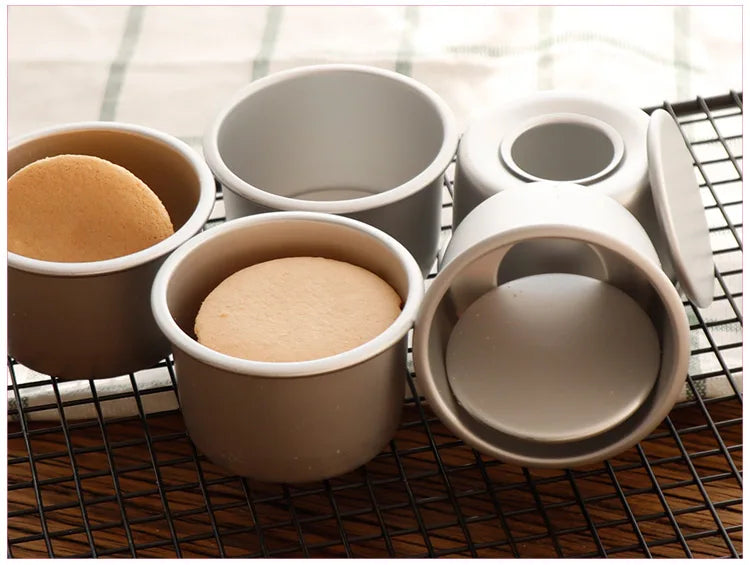 A set of five round non-stick cake molds in beige and gray are displayed on a black wire rack.