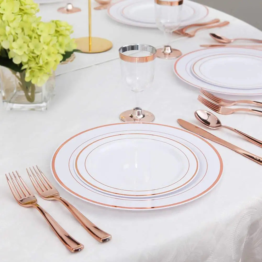 A white tablecloth set for a formal meal featuring gold disposable cutlery, plates, and glassware.