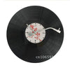 A black vinyl record is mounted on a wall clock with white markings and a silver hand.