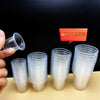 A hand holds a stack of clear, disposable mini tasting cups on a light surface against a black background.