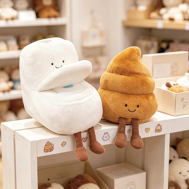 A white plush toy shaped like a toilet with a plunger, next to an orange plush toy shaped like a poop plunger.