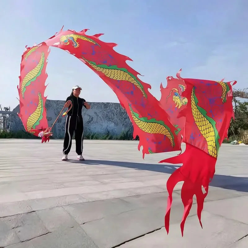 Una persona vestida de negro realiza una danza de dragón con grandes accesorios de tela roja y amarilla contra un fondo gris 