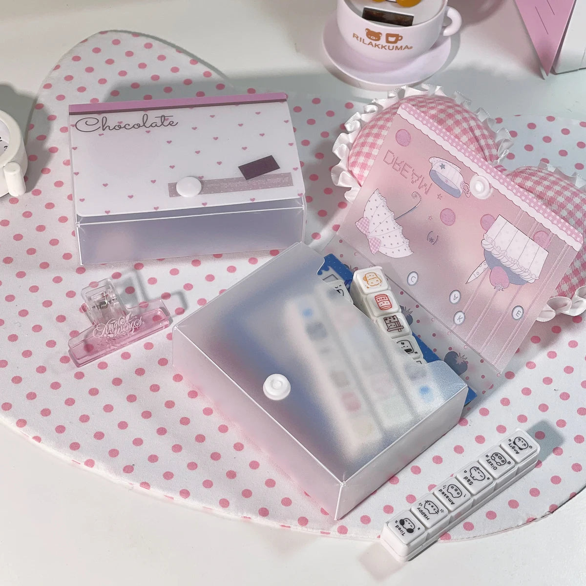 Una caja de almacenamiento minimalista rosa para pegatinas y tarjetas junto a una caja de chocolate y una taza blanca.