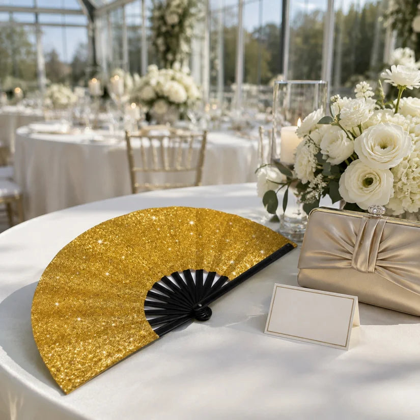 Gold and black foldable hand fans displayed on a white tablecloth at an outdoor event setting.