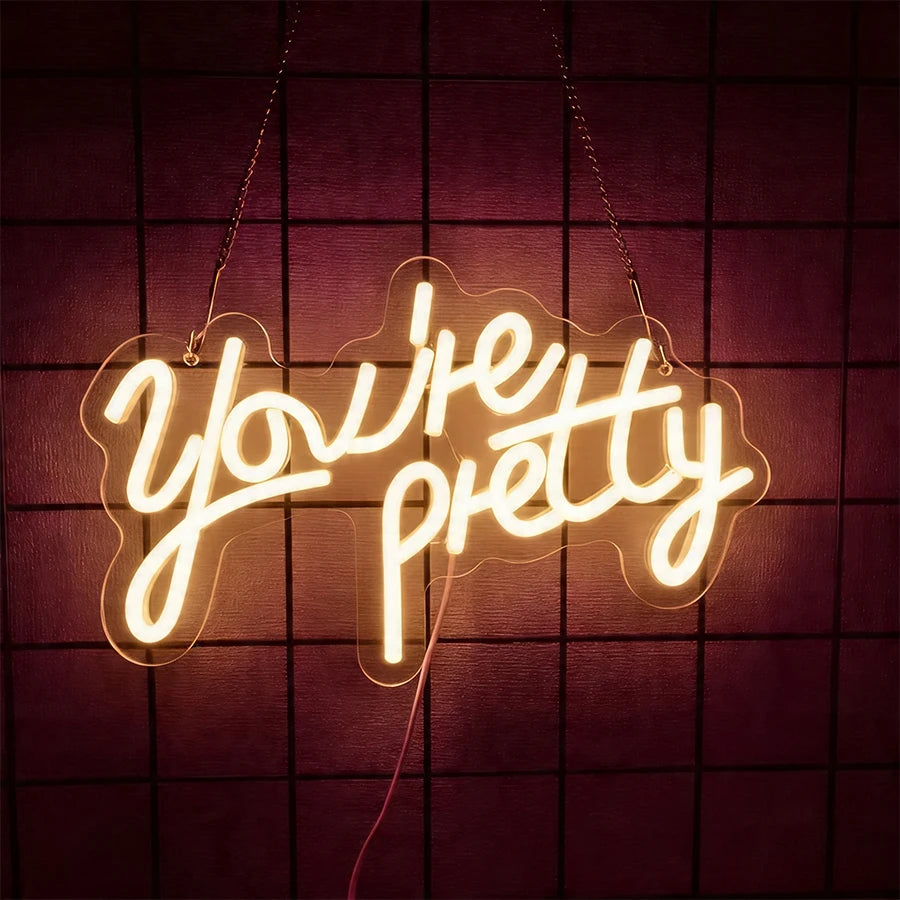 A glowing neon sign spelling out You're Pretty against a dark purple grid background.